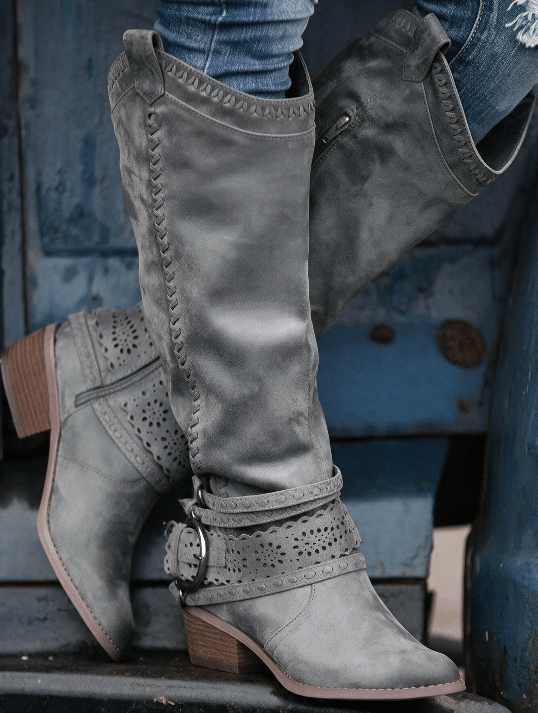 The Sloane Boots in grey suede — tall cut-out harness boot on rustic blue steps